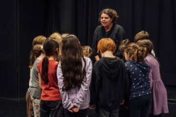viele Kinder-Schaspieler:innen stehen vor einer Schauspiellehrerin im Kreis